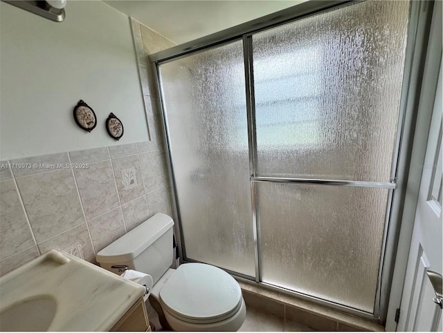 bathroom featuring a shower with door, vanity, tile walls, and toilet