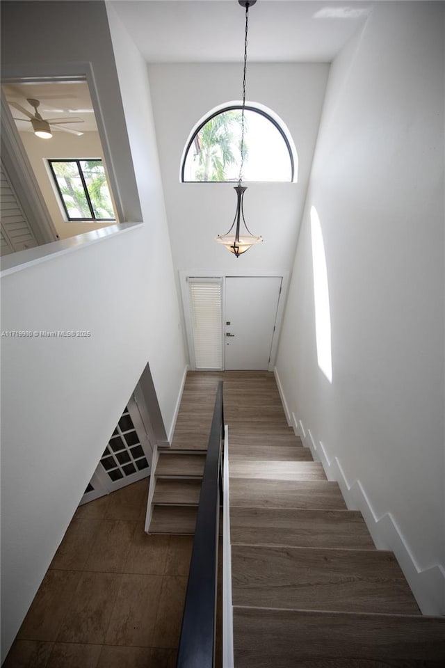 stairs featuring a towering ceiling, ceiling fan, and a healthy amount of sunlight