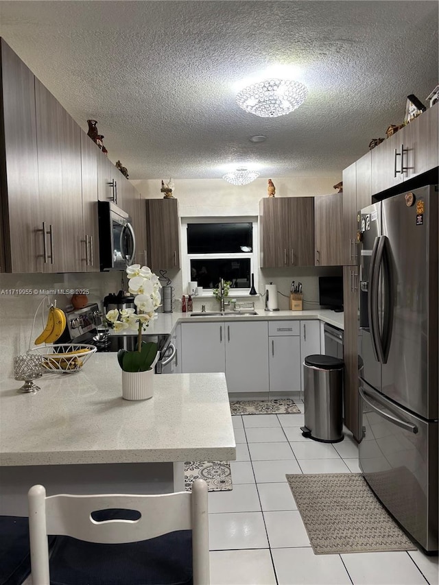 kitchen featuring sink, light tile patterned floors, a textured ceiling, dark brown cabinetry, and stainless steel appliances