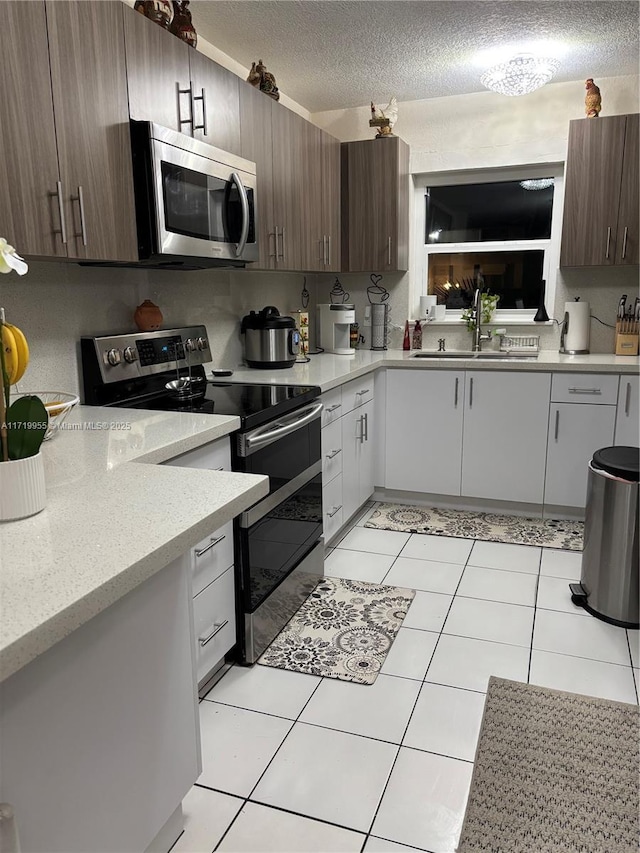 kitchen with dark brown cabinetry, sink, stainless steel appliances, a textured ceiling, and white cabinets