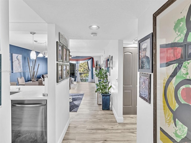 hallway featuring light wood finished floors, baseboards, and a textured ceiling