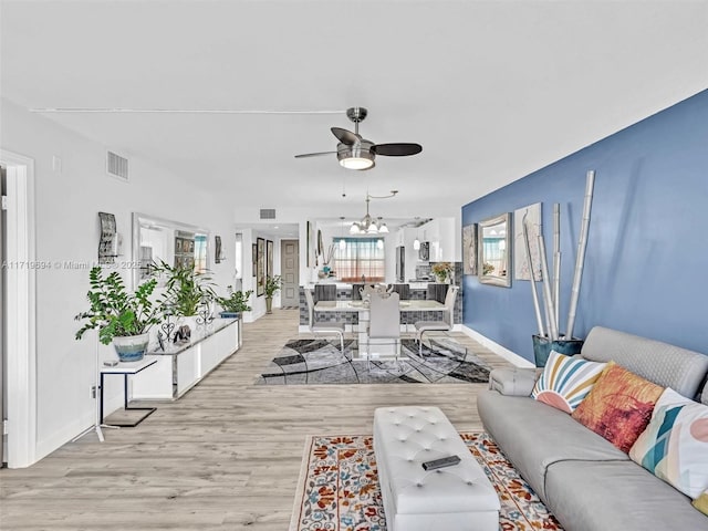 living room with light wood-style floors, baseboards, visible vents, and ceiling fan with notable chandelier