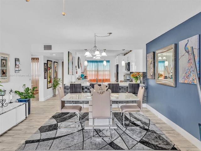 dining space featuring light wood-style flooring, visible vents, a chandelier, and baseboards