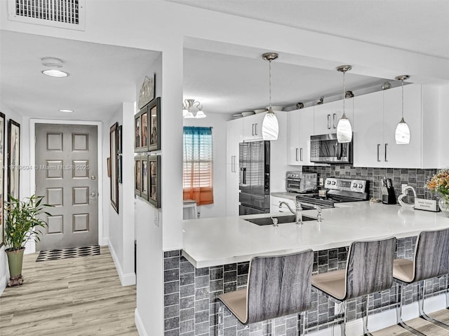 kitchen with light wood finished floors, tasteful backsplash, appliances with stainless steel finishes, a breakfast bar, and a peninsula