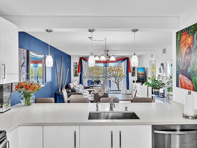 kitchen with white cabinetry, open floor plan, light countertops, stainless steel dishwasher, and hanging light fixtures