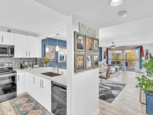 kitchen featuring a sink, stainless steel appliances, light countertops, light wood-style floors, and backsplash