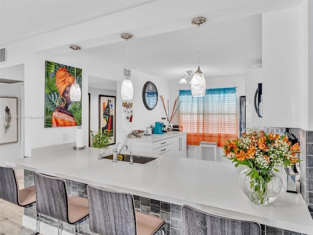 kitchen with white cabinets, a breakfast bar area, decorative light fixtures, a peninsula, and a sink