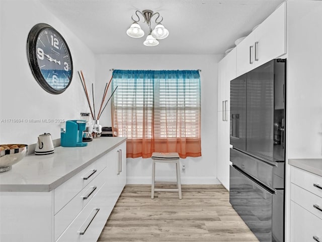 kitchen with baseboards, light wood-style flooring, freestanding refrigerator, white cabinetry, and a notable chandelier