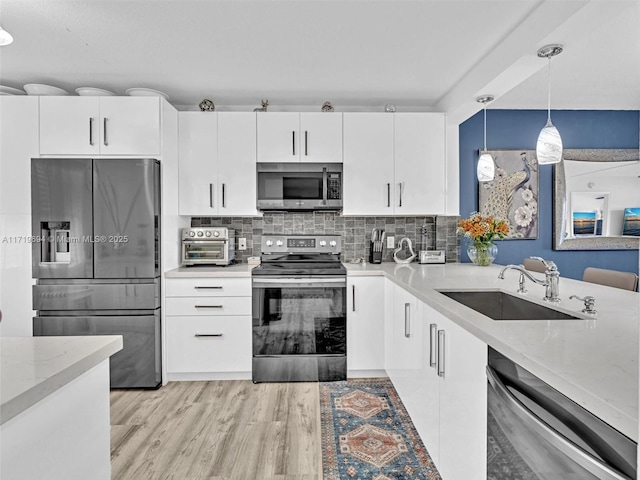 kitchen featuring stainless steel appliances, a sink, light wood-type flooring, decorative backsplash, and decorative light fixtures