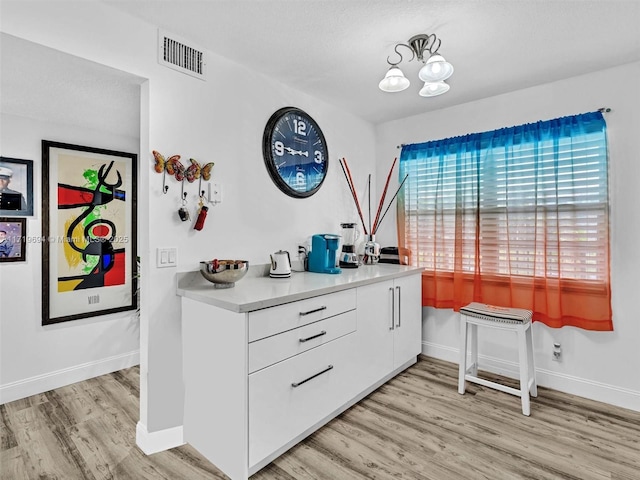 kitchen with light wood-style flooring, visible vents, baseboards, white cabinetry, and light countertops