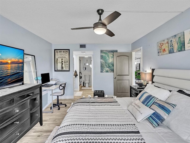 bedroom with a textured ceiling, ensuite bathroom, light wood-style flooring, a ceiling fan, and visible vents