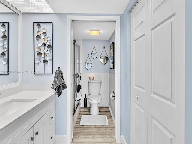 full bath featuring toilet, a wainscoted wall, wood finished floors, vanity, and walk in shower