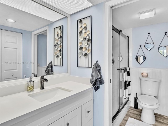 full bathroom featuring a stall shower, wainscoting, vanity, and wood finished floors