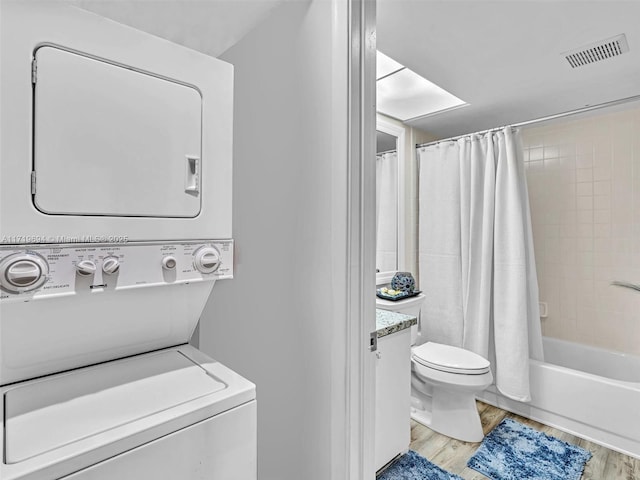 bathroom featuring visible vents, toilet, wood finished floors, vanity, and stacked washing maching and dryer