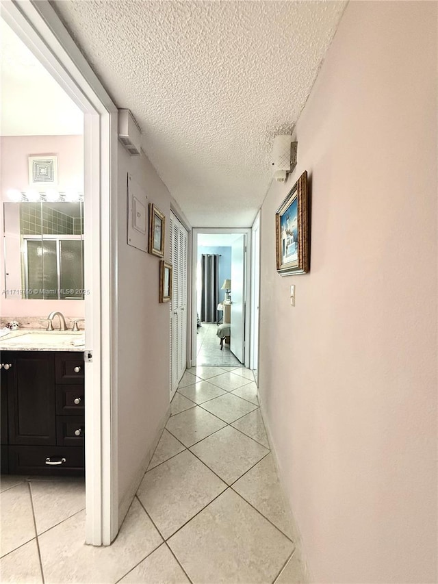 hallway with sink, light tile patterned floors, and a textured ceiling