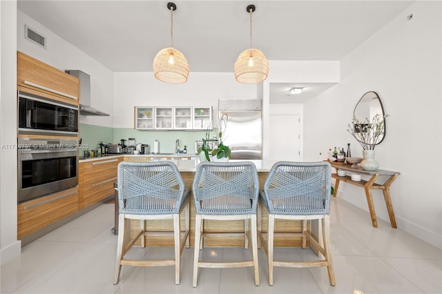 kitchen featuring backsplash, wall chimney range hood, light tile patterned floors, a center island, and built in refrigerator