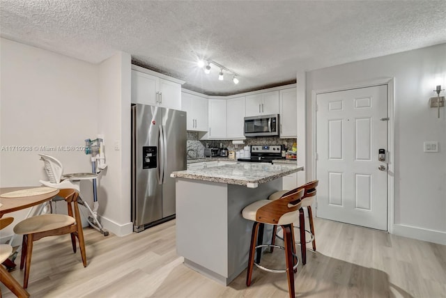 kitchen with tasteful backsplash, white cabinets, a kitchen breakfast bar, and appliances with stainless steel finishes