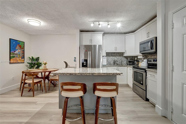 kitchen featuring white cabinetry, light stone countertops, stainless steel appliances, backsplash, and a kitchen island