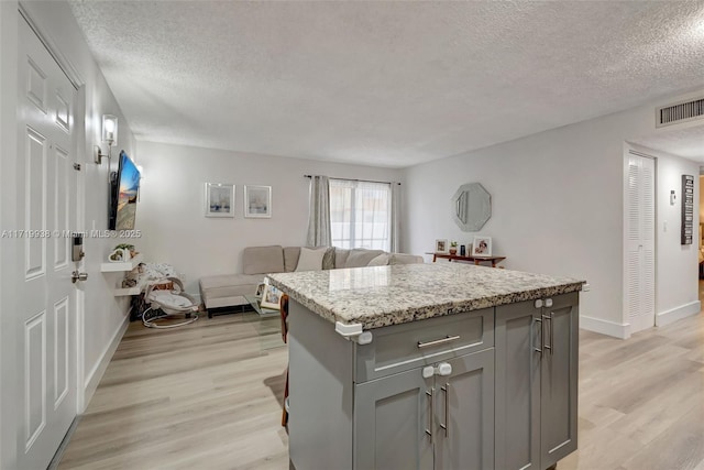 kitchen featuring a center island, light stone counters, a textured ceiling, gray cabinets, and light wood-type flooring