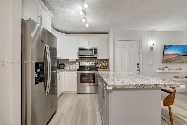 kitchen featuring appliances with stainless steel finishes, backsplash, a breakfast bar, white cabinets, and a center island