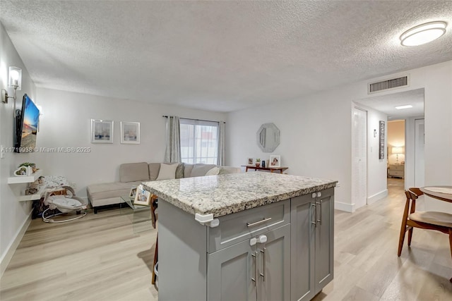 kitchen with gray cabinetry, light stone countertops, a center island, and light wood-type flooring