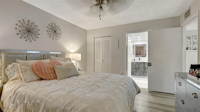 bedroom with ensuite bath, a textured ceiling, ceiling fan, light hardwood / wood-style flooring, and a closet