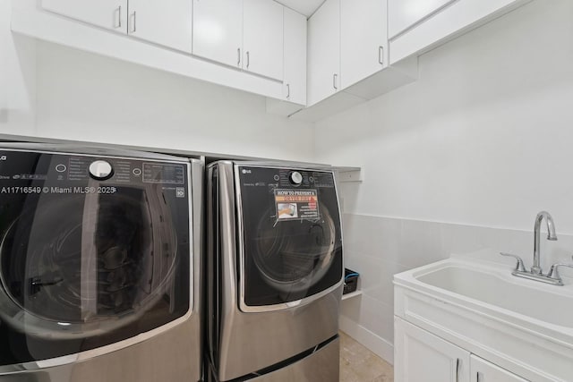 clothes washing area with tile walls, cabinets, separate washer and dryer, and sink