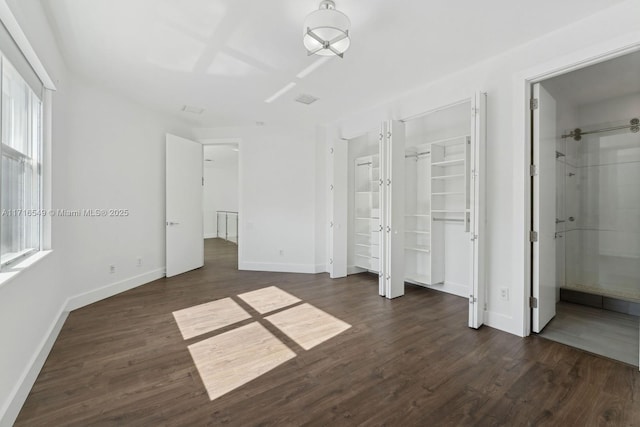 unfurnished bedroom featuring ensuite bathroom, dark hardwood / wood-style flooring, and multiple windows