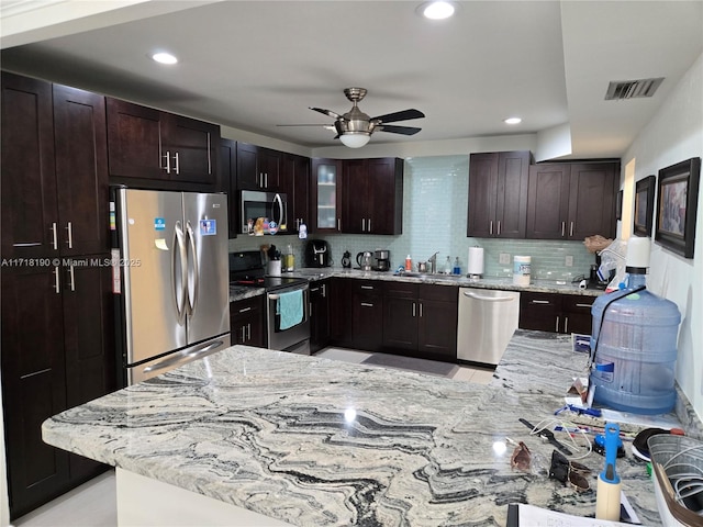 kitchen featuring decorative backsplash, light stone countertops, dark brown cabinetry, stainless steel appliances, and ceiling fan