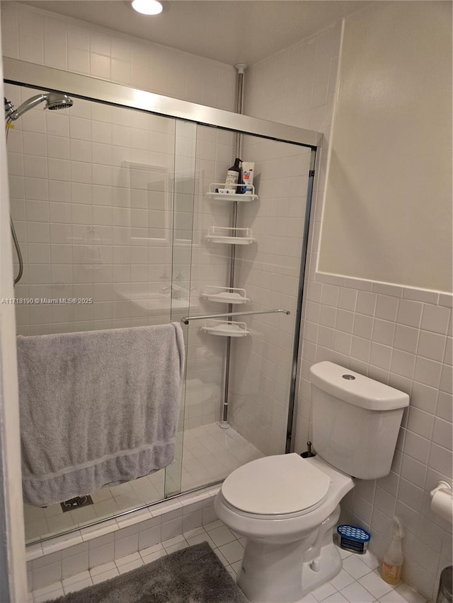 bathroom with toilet, tile patterned floors, a shower with door, and tile walls