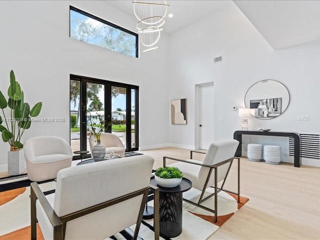 living room with a chandelier, french doors, a high ceiling, and light hardwood / wood-style flooring