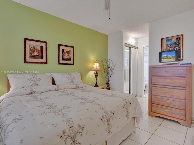 bedroom with light tile patterned floors, a closet, ensuite bath, and ceiling fan