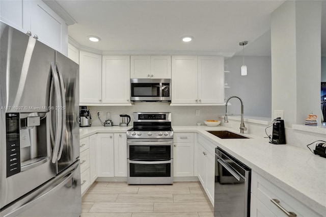 kitchen featuring light stone counters, stainless steel appliances, sink, white cabinetry, and hanging light fixtures