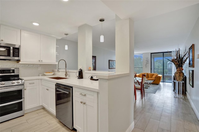 kitchen with sink, expansive windows, pendant lighting, white cabinets, and appliances with stainless steel finishes