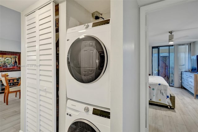 laundry area with light wood-type flooring, stacked washer / dryer, and ceiling fan