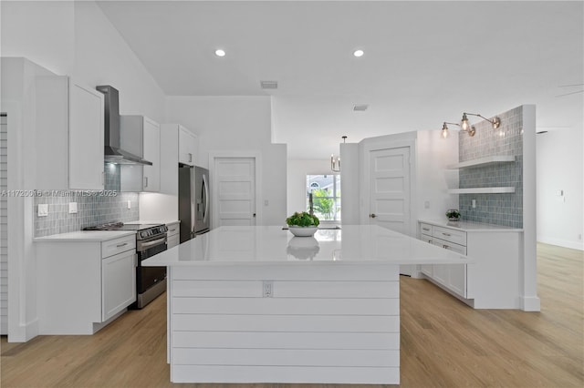 kitchen with backsplash, stainless steel appliances, wall chimney range hood, white cabinets, and light hardwood / wood-style floors