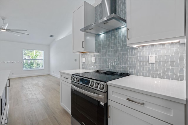 kitchen with backsplash, stainless steel range with electric cooktop, white cabinets, wall chimney range hood, and light wood-type flooring