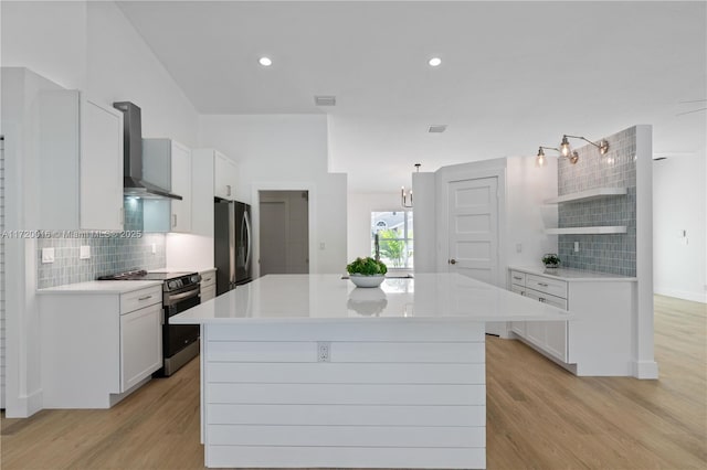 kitchen featuring white cabinetry, stainless steel appliances, wall chimney range hood, tasteful backsplash, and light hardwood / wood-style floors