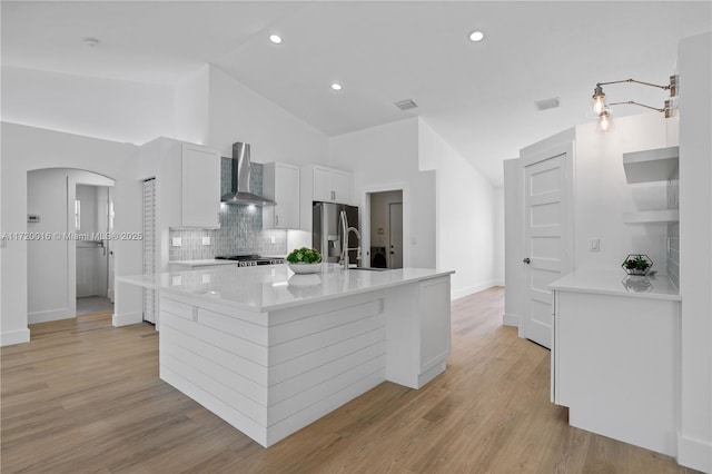 kitchen featuring tasteful backsplash, wall chimney range hood, a center island with sink, white cabinets, and stainless steel fridge with ice dispenser