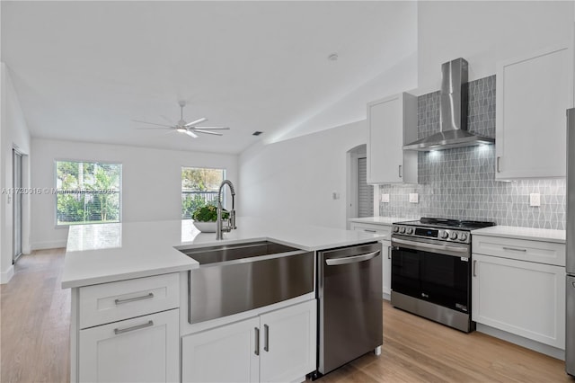 kitchen with sink, wall chimney range hood, vaulted ceiling, white cabinets, and appliances with stainless steel finishes