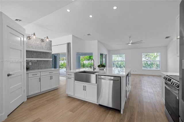 kitchen featuring backsplash, stainless steel appliances, a kitchen island with sink, ceiling fan, and white cabinetry