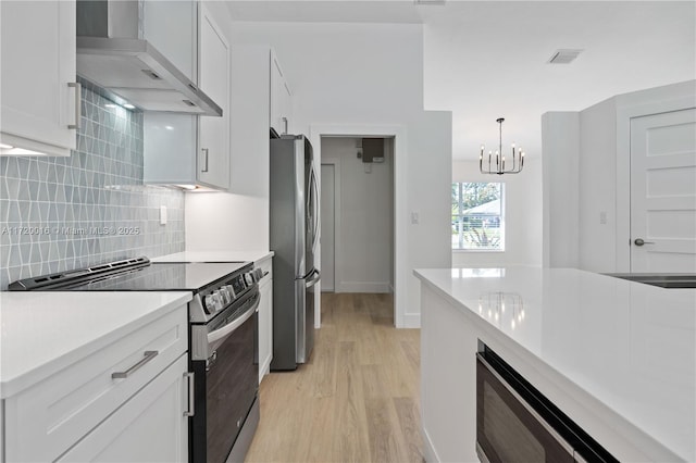 kitchen featuring light wood-type flooring, wall chimney exhaust hood, stainless steel appliances, white cabinetry, and hanging light fixtures