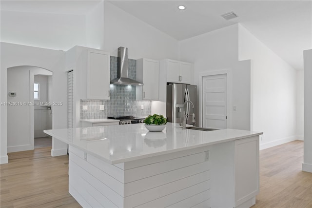 kitchen featuring white cabinetry, a kitchen island with sink, wall chimney exhaust hood, and stainless steel refrigerator with ice dispenser