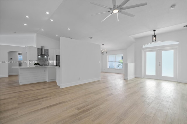 unfurnished living room with light hardwood / wood-style flooring, high vaulted ceiling, ceiling fan with notable chandelier, and sink