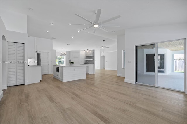 unfurnished living room with ceiling fan, sink, light hardwood / wood-style flooring, and vaulted ceiling