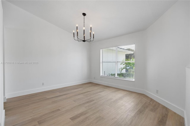 spare room with a notable chandelier and light wood-type flooring