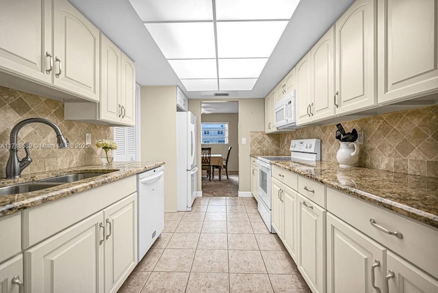 kitchen featuring white appliances, dark stone counters, white cabinets, sink, and light tile patterned flooring