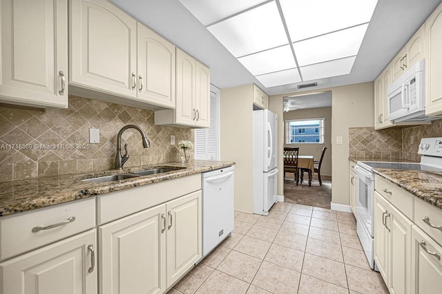 kitchen with dark stone counters, white appliances, sink, light tile patterned floors, and white cabinetry