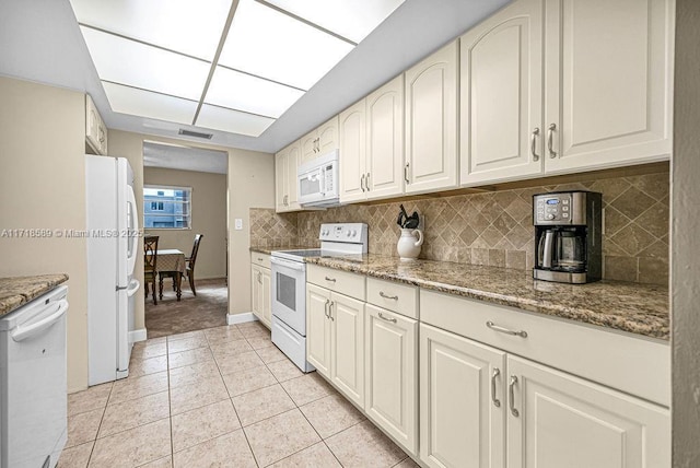 kitchen featuring tasteful backsplash, stone counters, light tile patterned floors, and white appliances