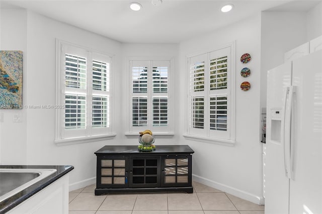 interior space with white cabinets, white fridge with ice dispenser, and light tile patterned flooring